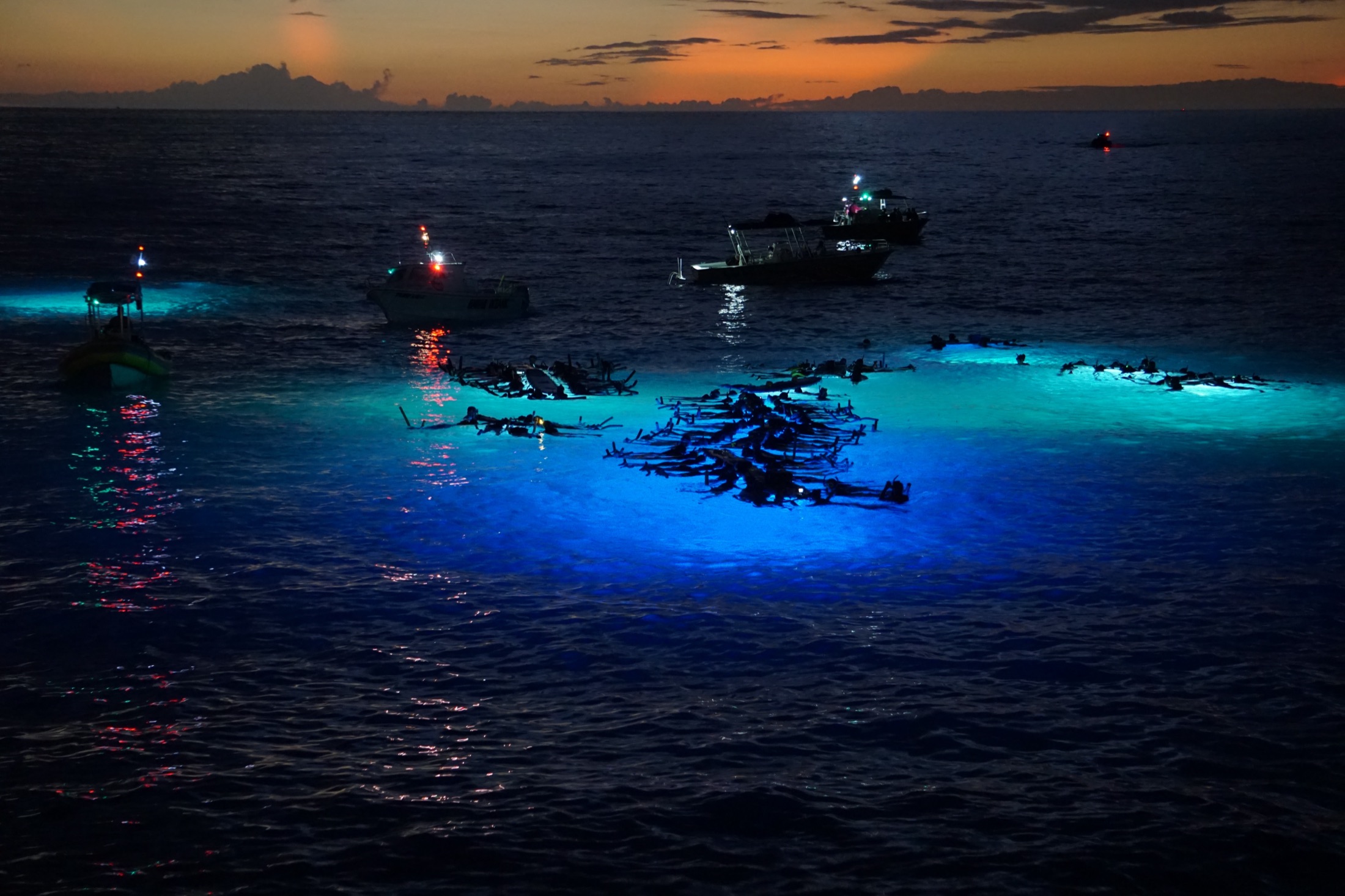 Dive lights glowing beneath snorkelers at dusk on the Kona coast