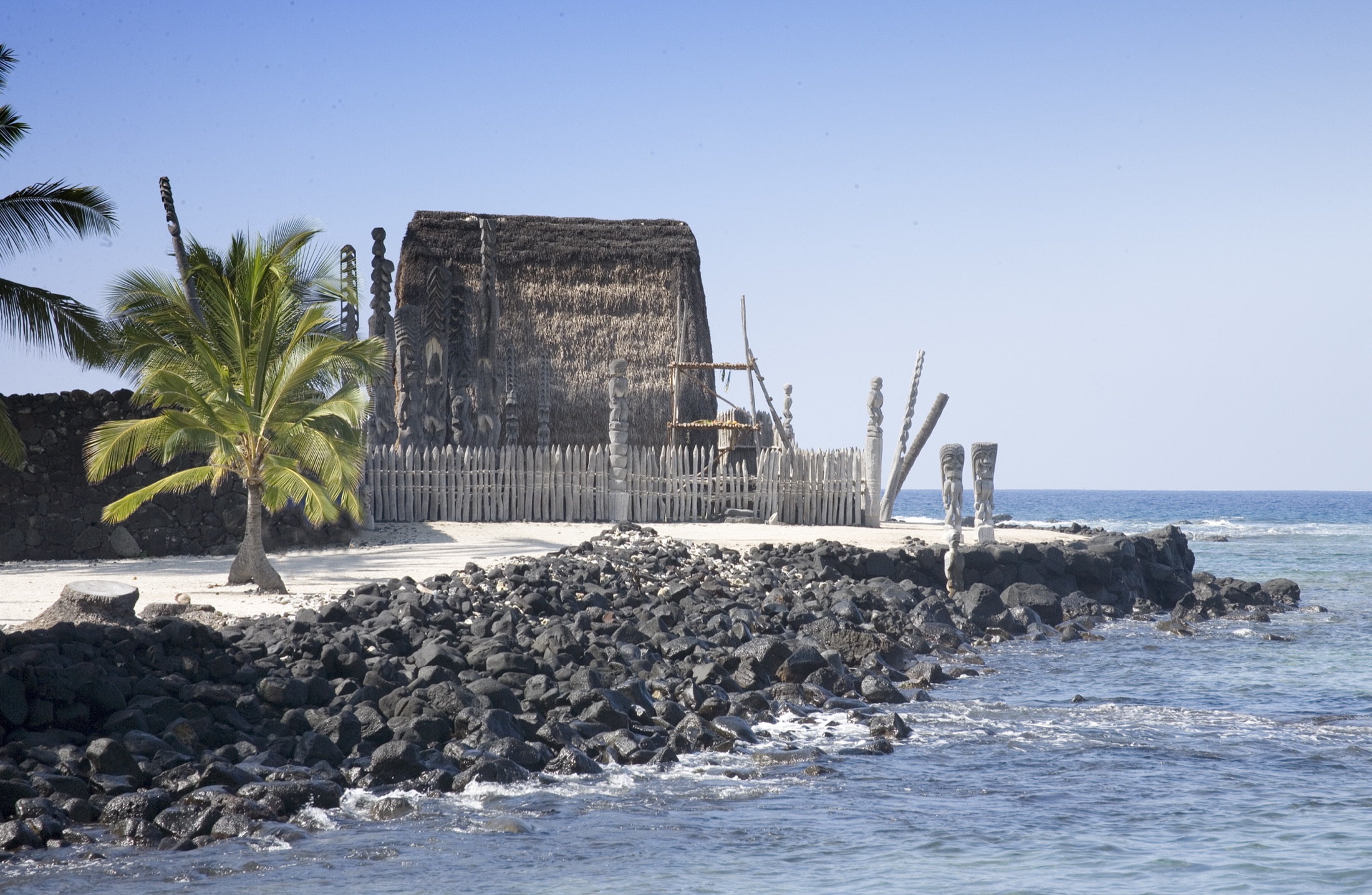 Carved kiʻi and the thatched hale at Puʻuhonua o Hōnaunau